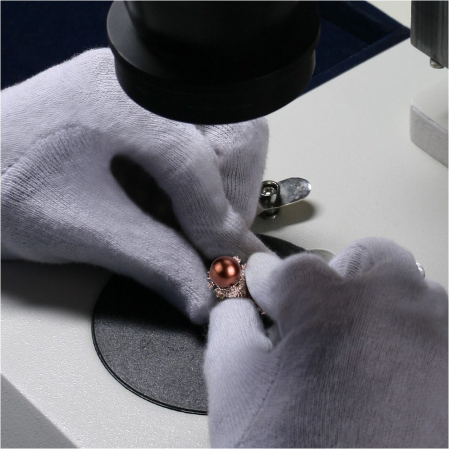 Gloved hands inspecting a finished ring under a microscope at the quality bench
